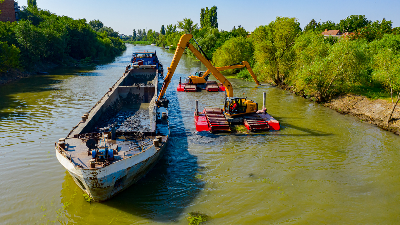 Above view on two excavators dredge as they dredging, working on river, canal, deepening and removing sediment, mud from riverbed in a polluted waterway.