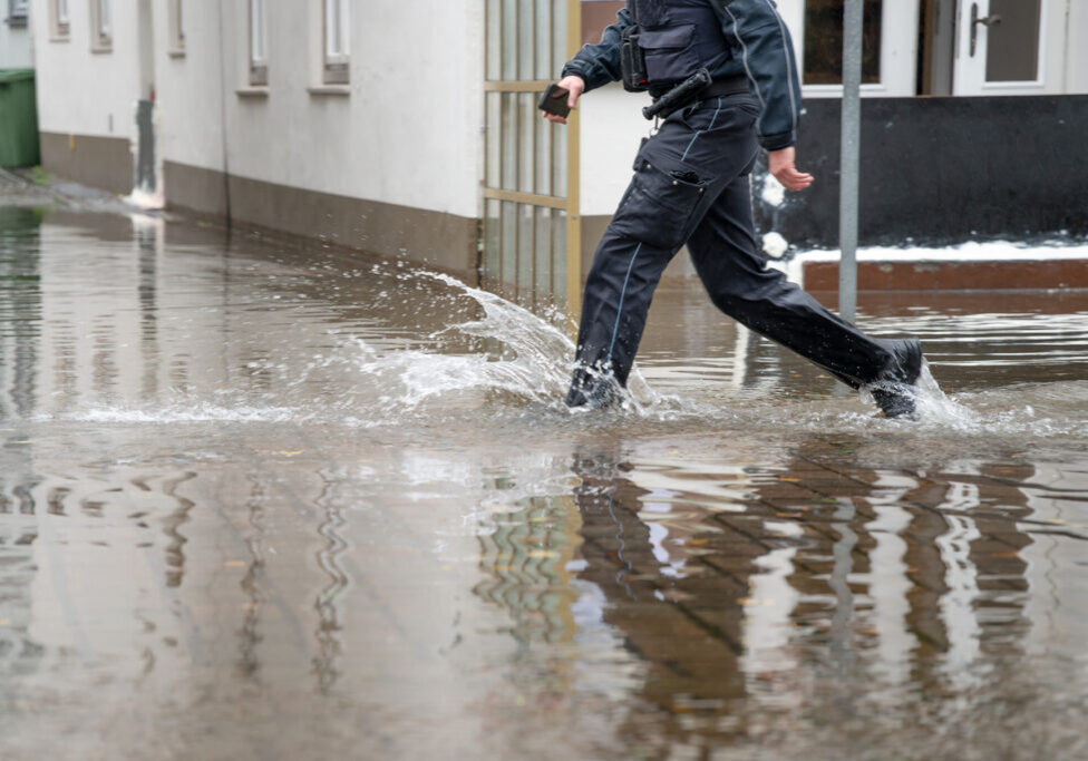 Policeman running through the water of a flooded street during high water of the river Trave in the old town of Lubeck at the Baltic sea in Germany, copy space, selected focus, motion blur