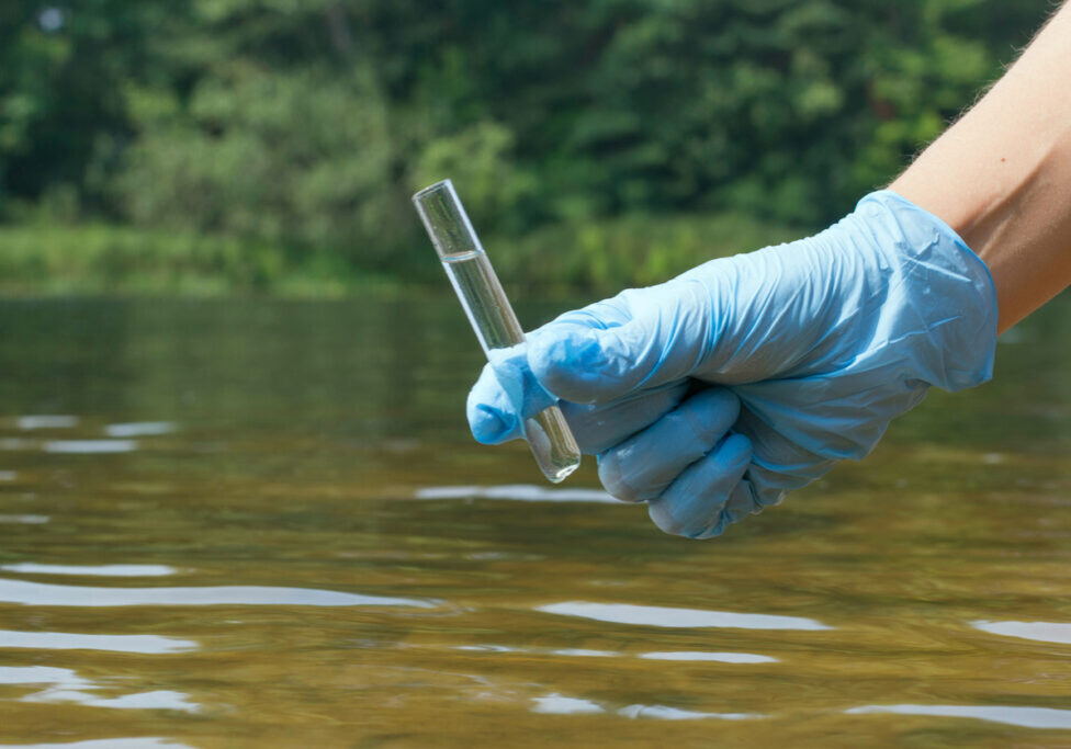 Sample water from the river for analysis. Hand in glove holding a test tube