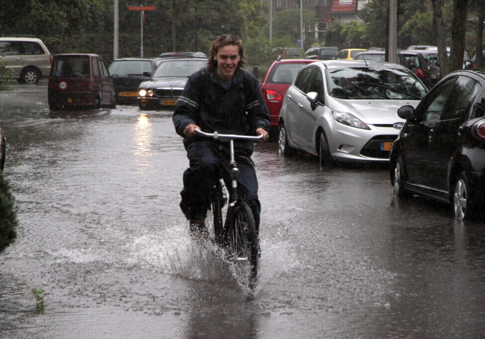 Oegstgeest, Netherlands - August 26, 2010: a young men riding a bicycle in a flooded street of a residential area.